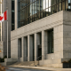 A modern Canadian bank facade with the national flag visible, photographed at eye level on a bright autumn day