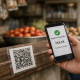 A smartphone displaying a mobile payment screen at a small Indian merchant stall with a QR code sticker
